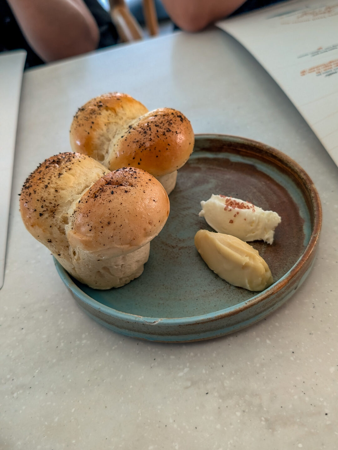 Two split milk bread rolls seasoned and served on a blue-rimmed ceramic plate alongside two scoops of house-churned flavored butter and coconut jam