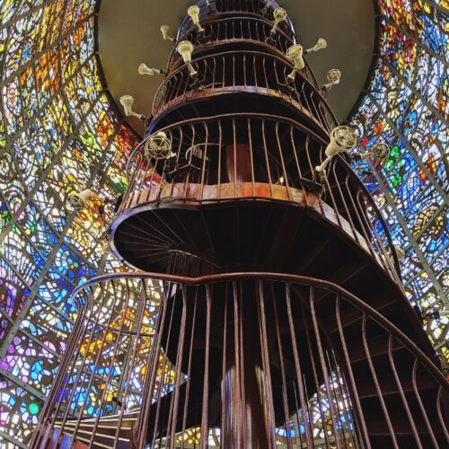 metal spiral staircase in a circular room surrounded by colorful stained glass windows