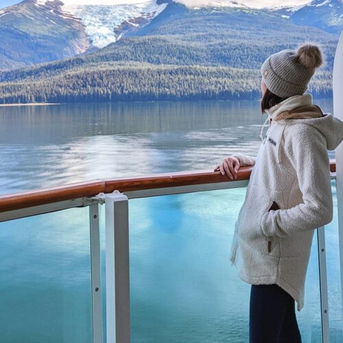 Gabi, The Fringe Explorer, looking out of a cruise ship balcony at a glacier sitting in a mountain