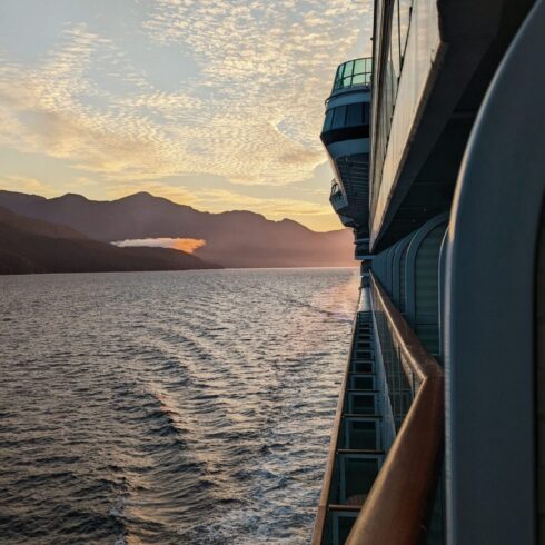 Looking off the side of a cruise ship balcony at the sunset. The sky is blue and yellow