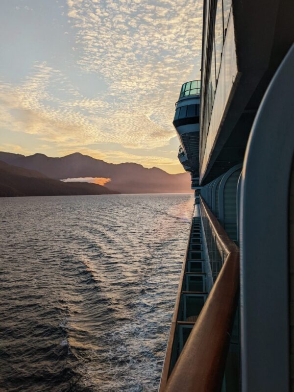 Looking off the side of a cruise ship balcony at the sunset. The sky is blue and yellow