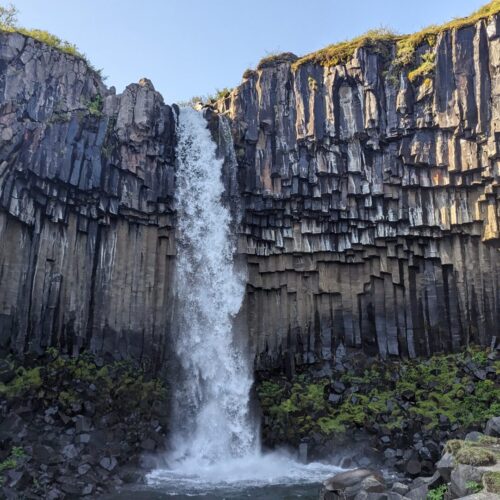 tall waterfall surrounded by brown basalt columns