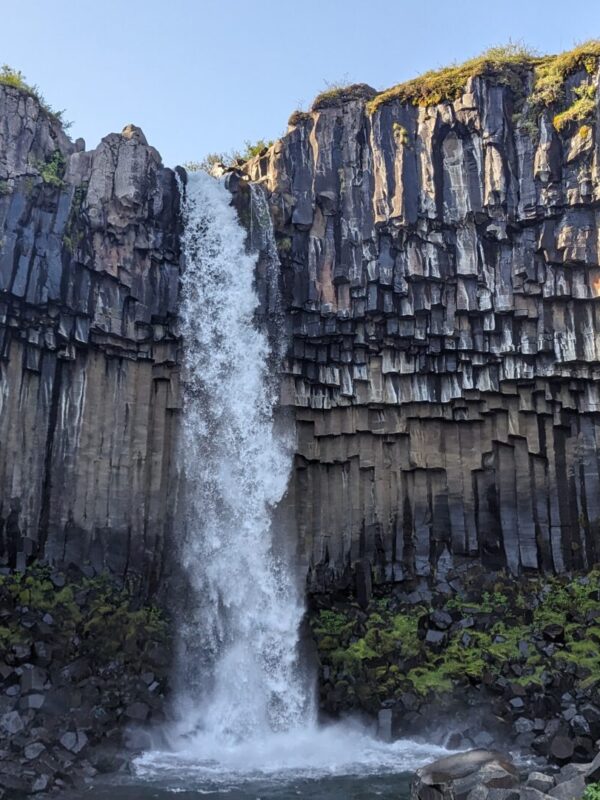 tall waterfall surrounded by brown basalt columns