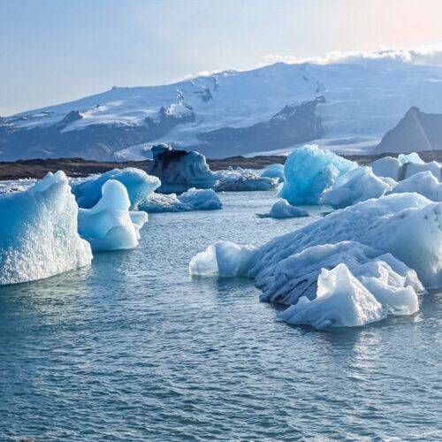 Glacier lagoon with large icebergs floating in the water. There are snow covered mountains in the background
