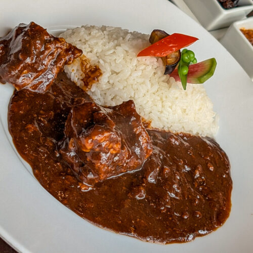 Rich Japanese beef curry with tender meat chunks served with white rice and fresh vegetable garnish at Nara Sanjo Curry.
